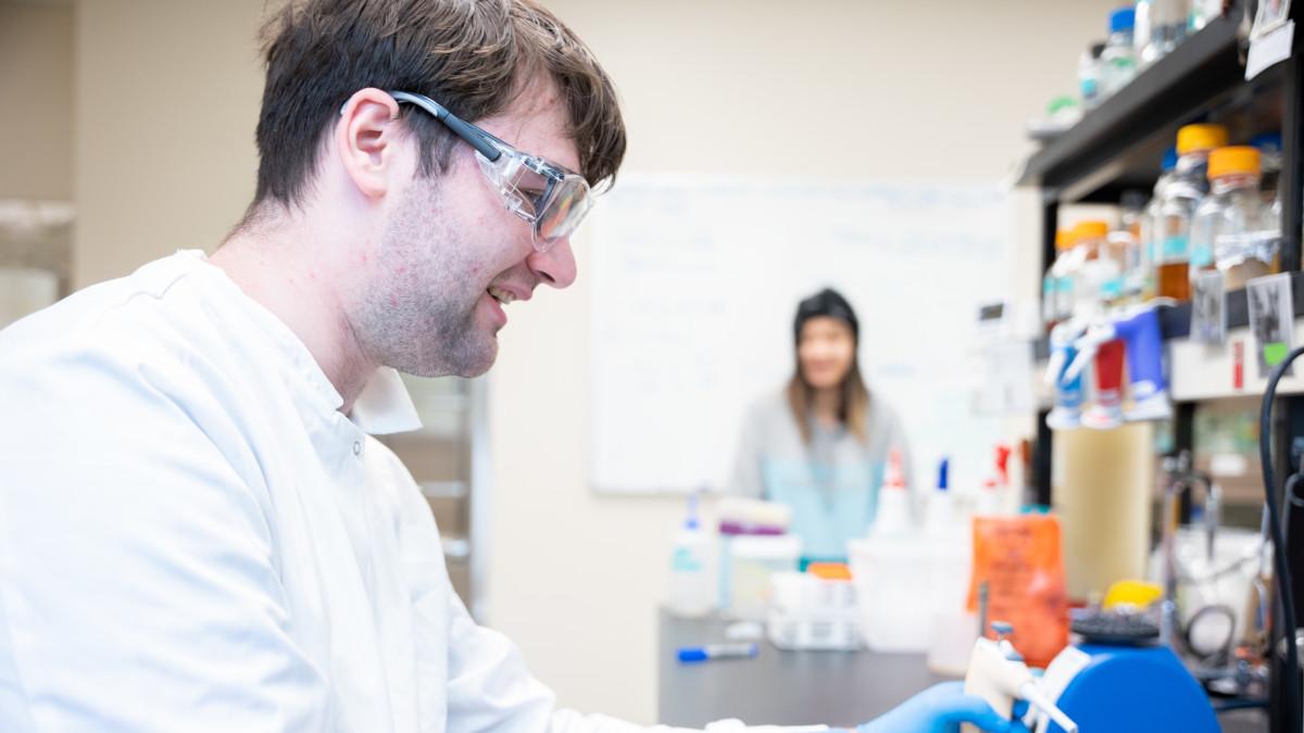 Smiling man wearing lab coat and safety glasses.