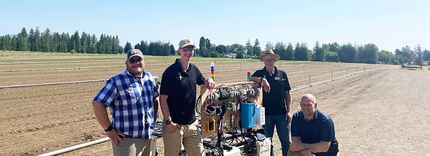 Four men pose with the weeding robot.